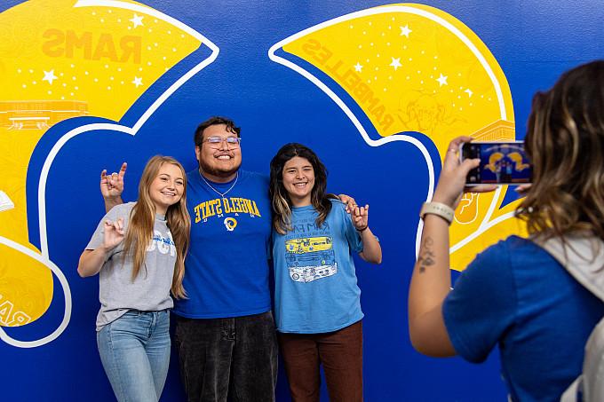 Angelo State students holding up the Ram Hand while having their photo taken.